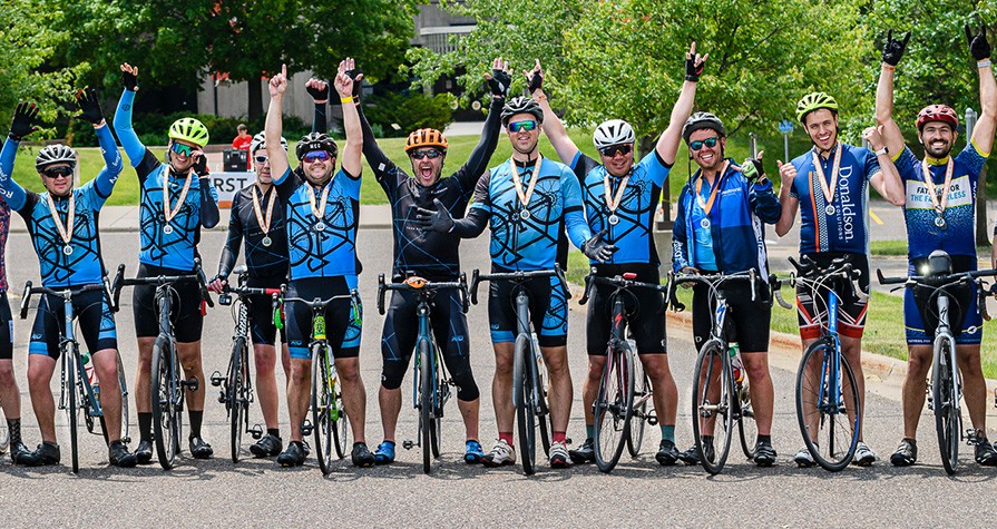 Row of people standing with their bikes with their arms raised smiling