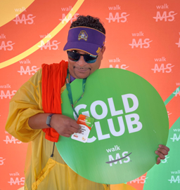 Man holding a Gold Club sign in front of Walk MS background