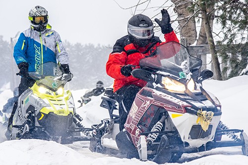 Two participants on snowmobiles wave