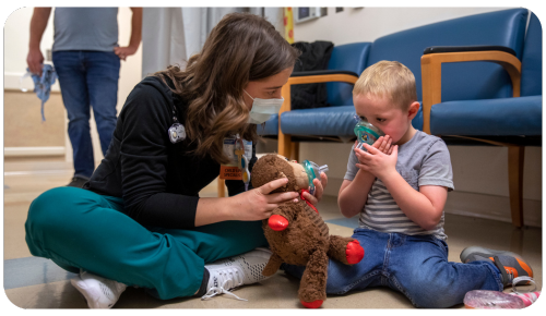 Penn State Health Child Life specialist Erin Palm shows Logan, a pediatric patient, how to properly wear his anesthesia mask by demonstrating with a stuffed monkey